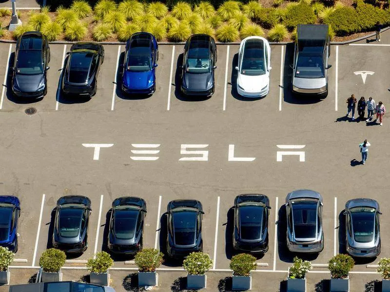 Park yerinde sıralanmış Tesla araçları ve zeminde büyük harflerle yazılmış Tesla adı.