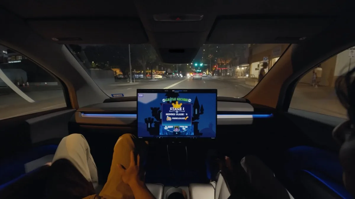Gece trafikte ilerleyen Tesla’nın içinden görünüm; orta ekranda harita, önde yol ve yolcuların bacakları görülüyor.