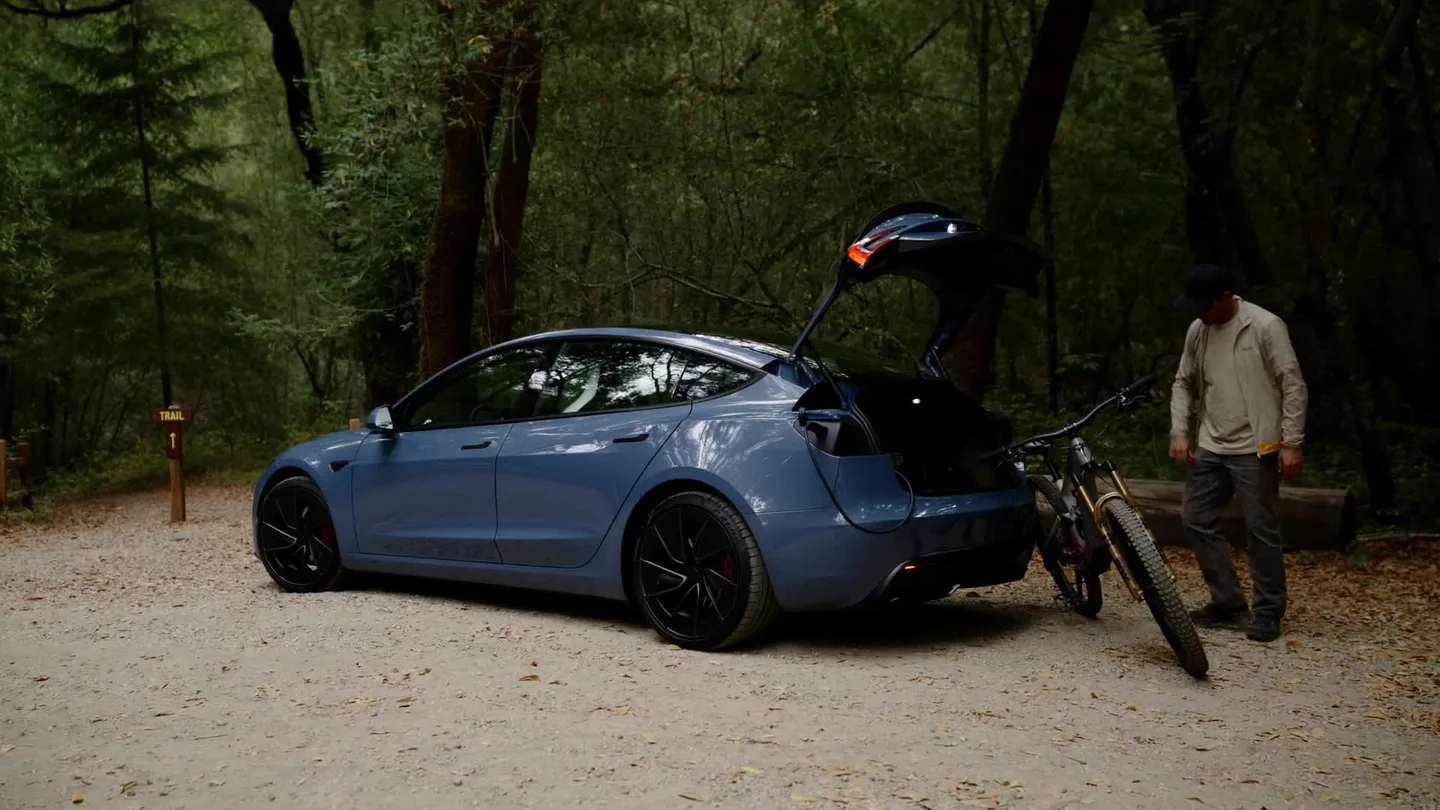 Açık bagaj kapağı ve yanında bir bisiklet bulunan mavi Tesla Model Y.