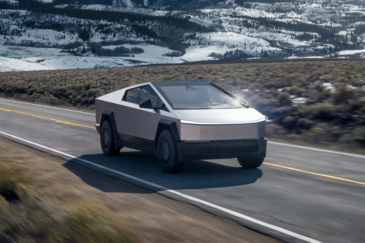 Karlı dağların önündeki bir yolda ilerleyen Tesla Cybertruck.