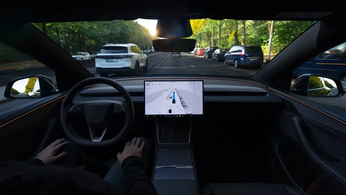 Tesla’nın ön koltuklarından görünen iç mekân; direksiyon, orta ekran ve ekranda araç ile yol şeritlerini gösteren sürüş arayüzü.