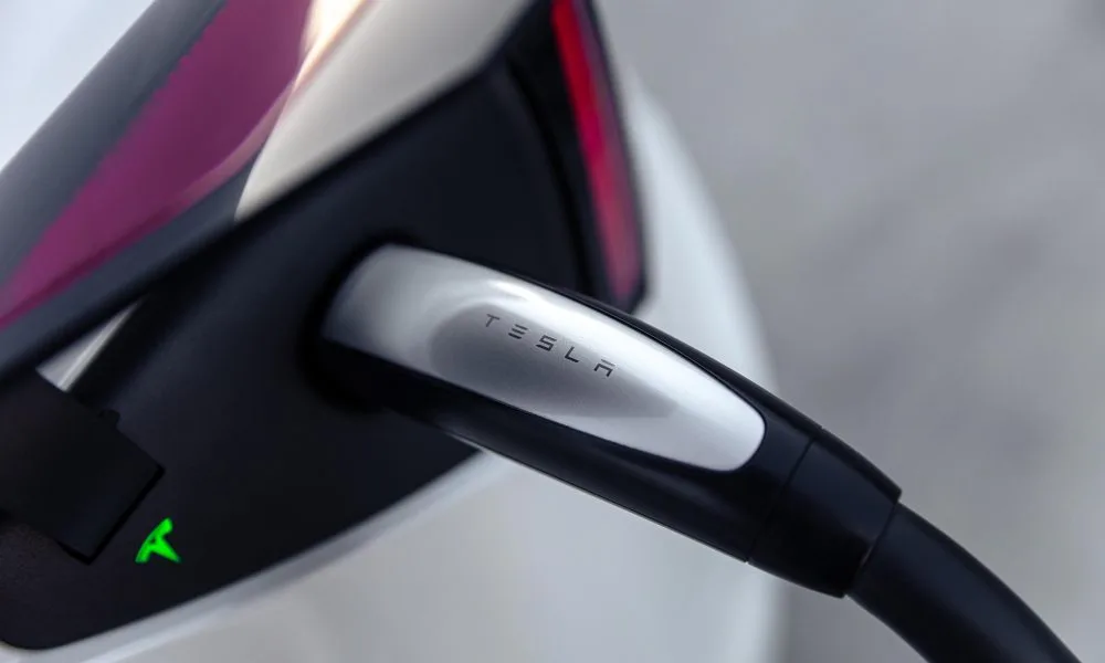 Tesla Supercharger kablosu, bir Tesla aracın şarj girişine takılı halde yakın planda görülüyor.
