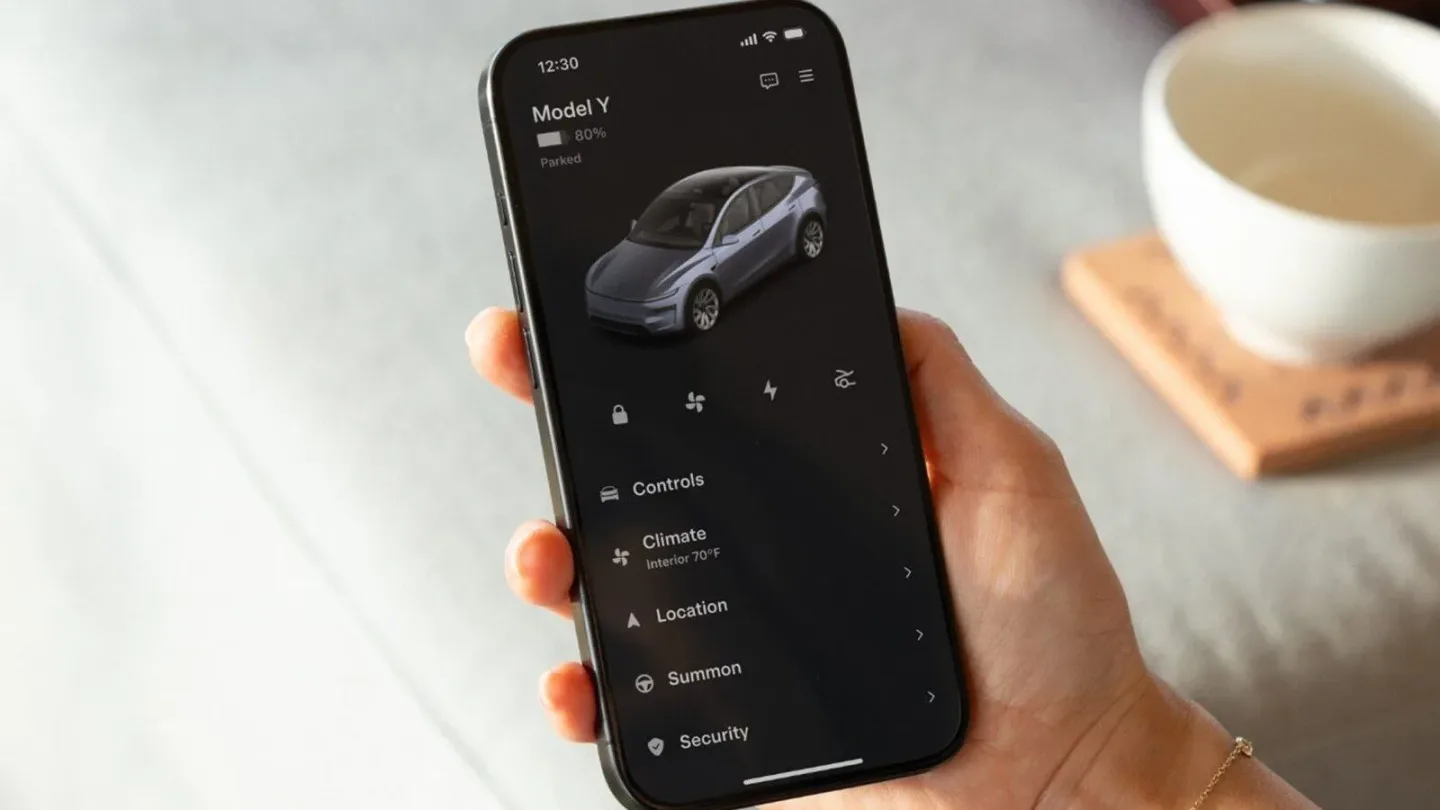 Bir elde tutulan telefonda Tesla uygulaması ve Model Y’ye ait araç kontrolü ile güvenlik menüleri görülüyor.